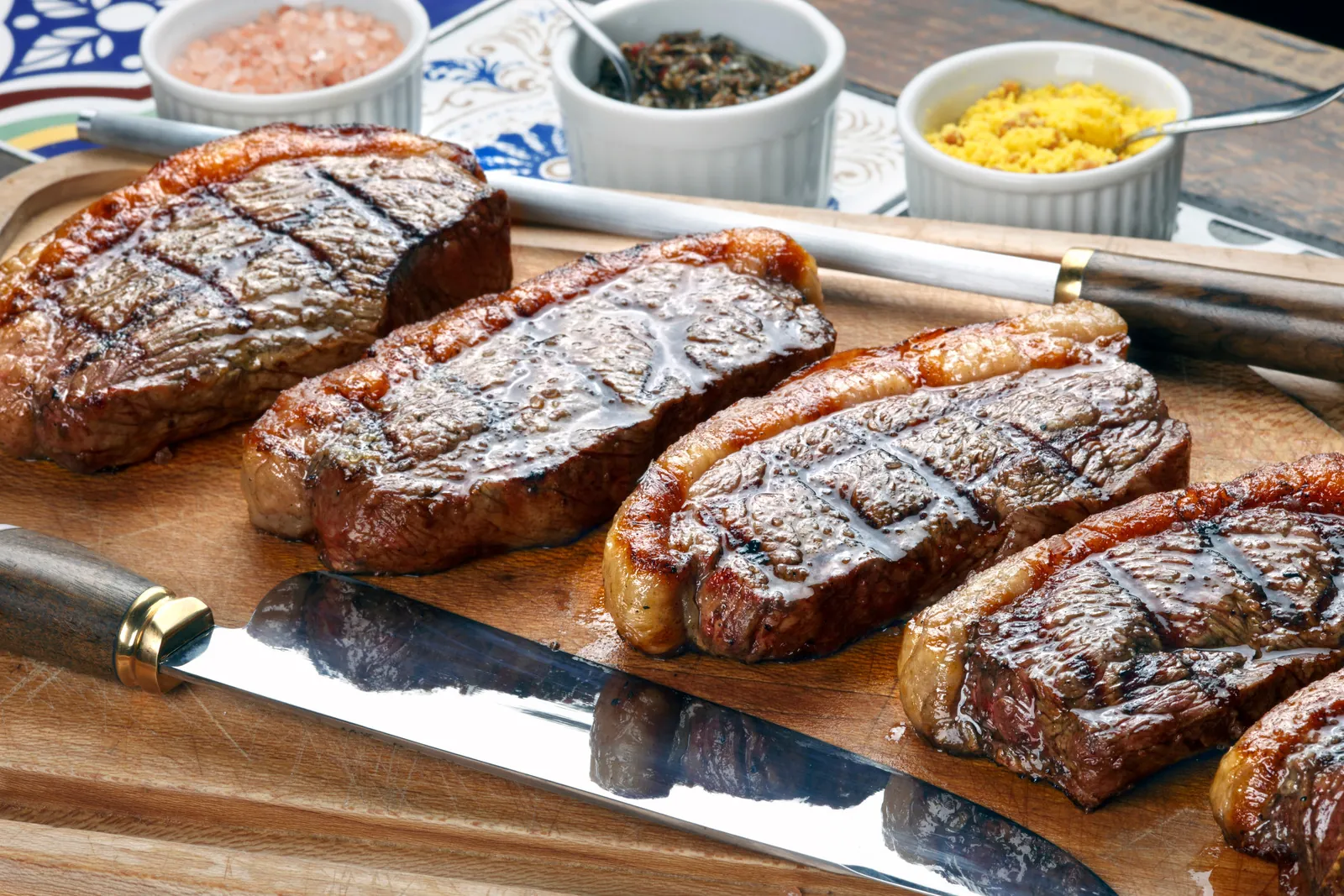 Grilled picanha steaks resting on a wooden board beside churrasco skewers